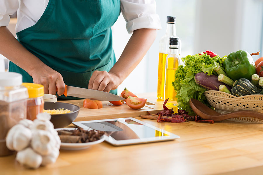 Cutting tomatoes on a cutting board surrounded by fruits and vegetables