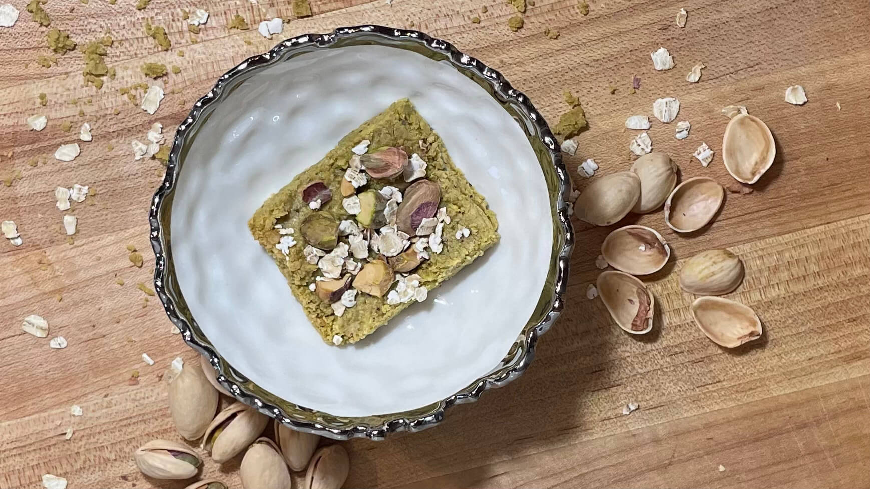 Picture of oat bar with pistachios in a white bowl, surrounded by pistachio shells. 