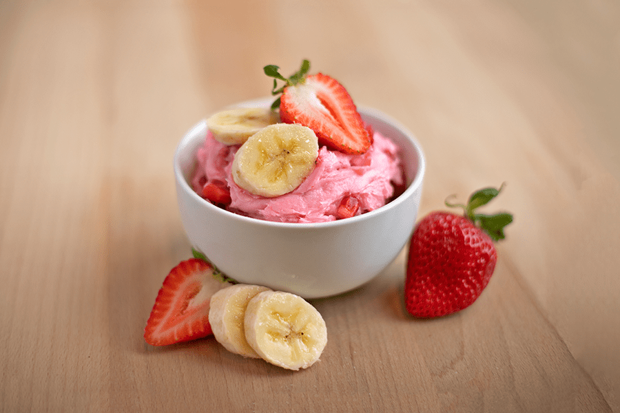 bowl of pink ice cream garnished with bananas and strawberries